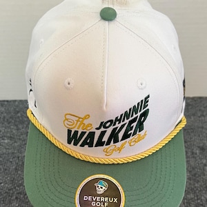 May include: White and green baseball cap with the text "The Johnnie Walker Golf Club" in gold and green. The cap has a green brim and a gold rope detail. A small green button is on top.