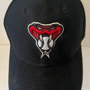 May include: A black baseball cap featuring an embroidered logo of a red snake with white fangs biting into a white baseball with black stitching. The cap has a structured crown and a curved brim, with a small black button at the top center.