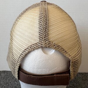 Op de afbeelding: Een bruine en beige truckerpet, van achteren gezien, met een mesh rug en een effen voorkant. De pet heeft een bruine verstelbare band en een bruine knoop aan de bovenkant. De mesh is beige en de effen voorkant is bruin.