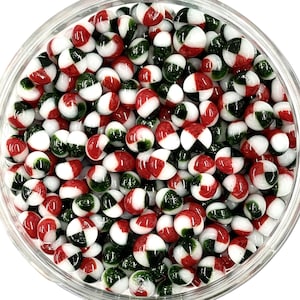 May include: A bowl filled with small, round, glass beads. The beads are white, red, and green, and have a speckled pattern.