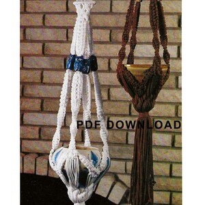 May include: Two macrame plant hangers, one white with blue beads and one brown with beige beads. Both hangers are hanging from a brick wall.