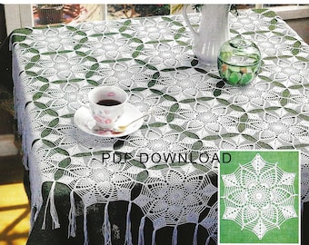 May include: White crochet tablecloth with a delicate floral pattern and fringe. The tablecloth is laid over a green table with a cup of coffee and a glass jar on top. A smaller white crochet doily is shown in the bottom right corner.