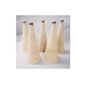 May include: A set of five beige, cone-shaped textile bobbins, each featuring a textured, fibrous surface and a single thin black horizontal stripe near the pointed top. These conical objects are arranged in a cluster, standing upright on their bases.