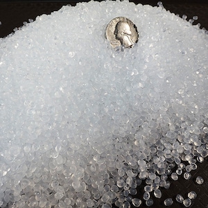 May include: A close-up of a pile of clear plastic pellets. A US quarter is included for scale.