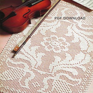 May include: A white crocheted doily with a floral design. The doily is laid out on a pink surface with a violin and sheet music on top of it. The text "PDF DOWNLOAD" is visible in the image.