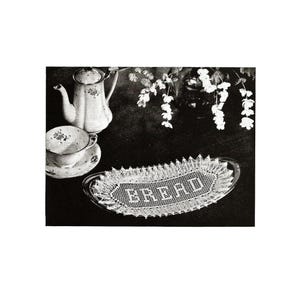 May include: A vintage still life featuring a tea set and a bread tray. The tea set includes a teapot, teacup, and saucer with floral designs. The bread tray is oval-shaped with the word "BREAD" embroidered on it. The background is dark.