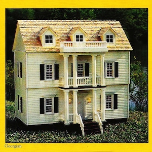 May include: A white two-story dollhouse with a brown shingled roof, white columns, and black shutters. The dollhouse has a front porch with a railing and steps. The dollhouse is surrounded by green grass.