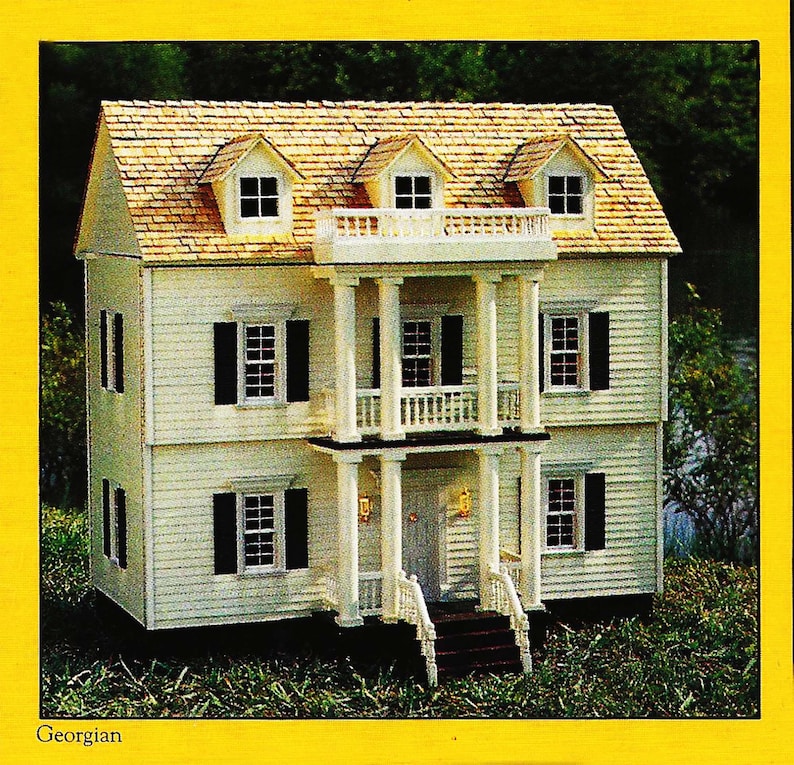 May include: A white two-story dollhouse with a brown shingled roof, white columns, and black shutters. The dollhouse has a front porch with a railing and steps. The dollhouse is surrounded by green grass.