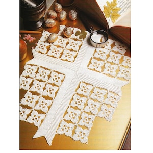 Puede incluir: Un tapete blanco de ganchillo con un diseño en forma de cruz. El tapete presenta un patrón floral repetido y un borde texturizado. La imagen también incluye elementos decorativos como huevos dorados, un mortero y una maja, y una lupa.