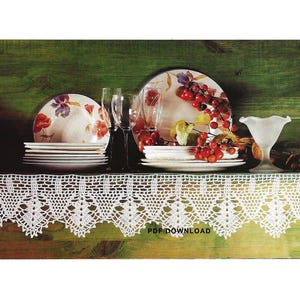 Könnte beinhalten: Eine weiße Häkelspitze mit einem gewellten Rand liegt auf einer grünen Holzoberfläche. Auf der Oberfläche befindet sich ein Stapel weißer Teller mit einem Blumendesign sowie eine Glasvase gefüllt mit roten Beeren.