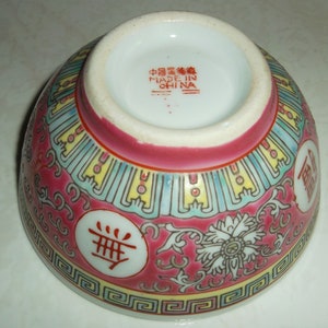 May include: A red and white porcelain bowl with a floral design and Chinese characters. The base of the bowl is marked "Made in China".
