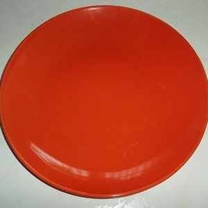 May include: A bright orange ceramic plate. The plate is round and has a smooth, glossy finish.
