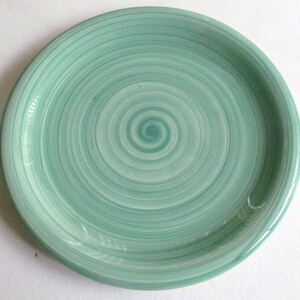 Puede incluir: Un plato de cerámica verde con un patrón de espiral. El plato tiene un acabado liso y brillante.