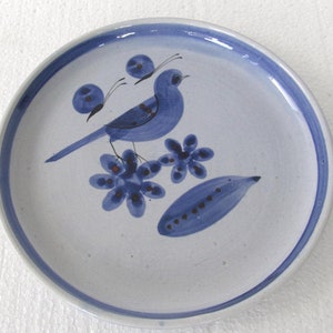May include: A blue and white ceramic plate with a blue bird design. The bird is perched on a branch with blue flowers. The plate has a white background with a blue rim.