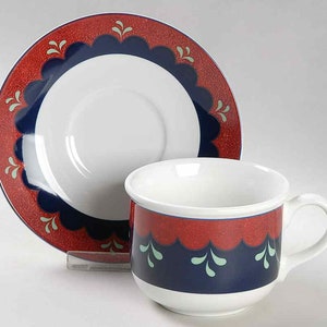 May include: A white teacup and saucer with a red, blue, and green floral pattern. The saucer has a scalloped edge.