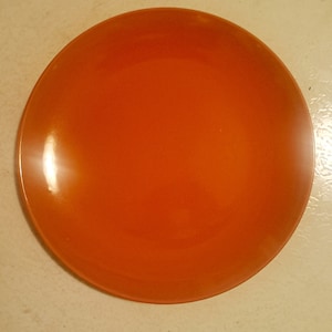 Pode incluir: Um prato de cerâmica laranja brilhante. O prato é redondo e tem um acabamento liso e brilhante.