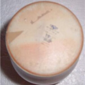 May include: The bottom of a round, cream-colored ceramic bowl with a light brown glaze. The bowl has a small, blue and white sticker with the text "Made in Italy" and a handwritten signature.