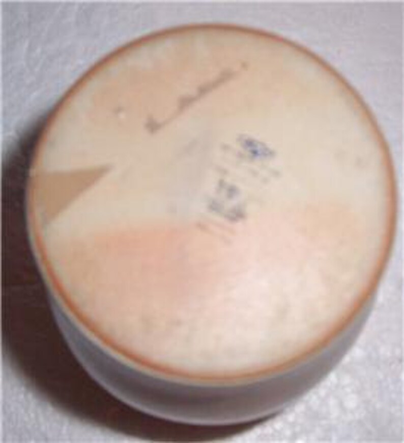 May include: The bottom of a round, cream-colored ceramic bowl with a light brown glaze. The bowl has a small, blue and white sticker with the text "Made in Italy" and a handwritten signature.