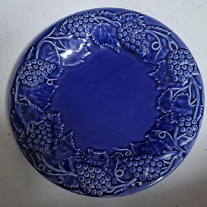 May include: A blue ceramic plate with a raised design of grapes and vines around the edge.