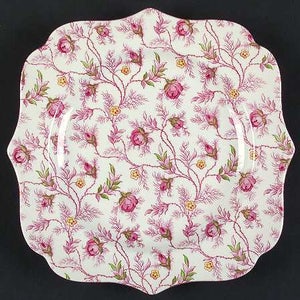 May include: A white ceramic serving platter with a scalloped edge. The platter features a pink and white floral pattern with a delicate vine design.