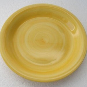 May include: A round, yellow ceramic plate with a slightly raised rim. The plate's surface features a spiral pattern of varying shades of yellow, creating a textured appearance. The plate is designed for serving food.