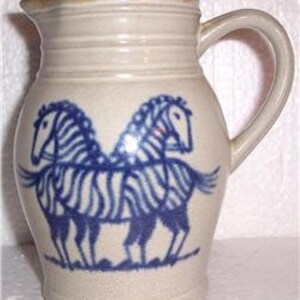 May include: A ceramic pitcher with a blue and white zebra design. The pitcher has a rounded body and a handle.