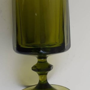 May include: A dark green glass goblet with a wide base and a fluted design. The goblet is empty and has a clear, reflective surface.