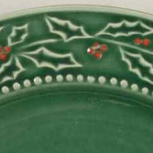 May include: A green ceramic plate with a white holly leaf design and red berries around the rim.