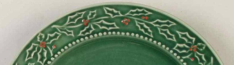 May include: A green ceramic plate with a white holly leaf design and red berries around the rim.