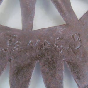 May include: Close-up of a rusty metal starburst with the word "J.VADER" inscribed on the surface.