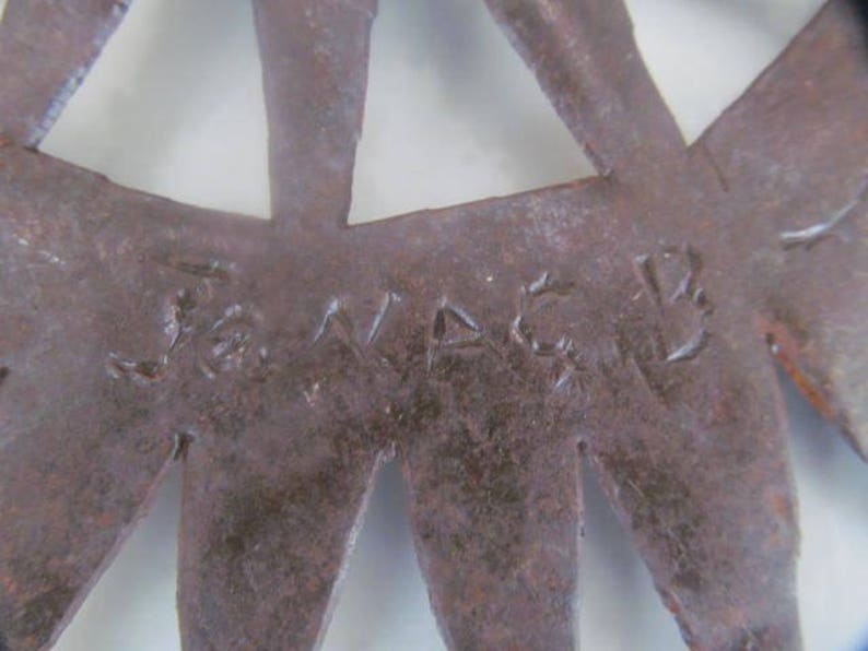 May include: Close-up of a rusty metal starburst with the word "J.VADER" inscribed on the surface.