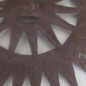 May include: A rusty metal sunburst wall decor with a starburst design and a raised centre. The piece is signed "Fort Worth" in the lower right corner.