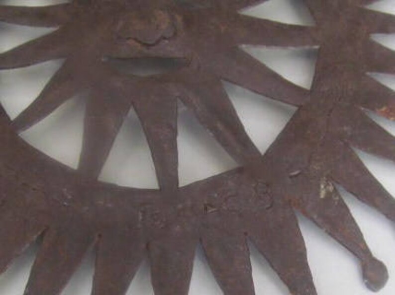May include: A rusty metal sunburst wall decor with a starburst design and a raised centre. The piece is signed "Fort Worth" in the lower right corner.