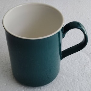 Op de afbeelding: Een tealgroene keramische mok met een witte binnenkant. De mok heeft een afgeronde handgreep.