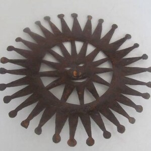 May include: A rusty metal sun with a smiling face and a crown of points around the edge.