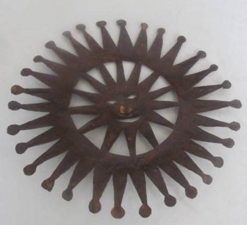 May include: A rusty metal sun with a smiling face and a crown of points around the edge.