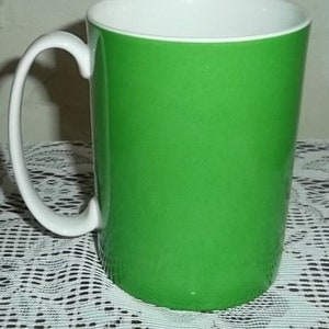 May include: A green ceramic mug with a white handle. The mug is sitting on a white and black patterned surface.