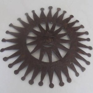 May include: A metal sun with a face and 16 rays, each with a pointed tip. The sun is a cutout design, with the face visible through the centre.