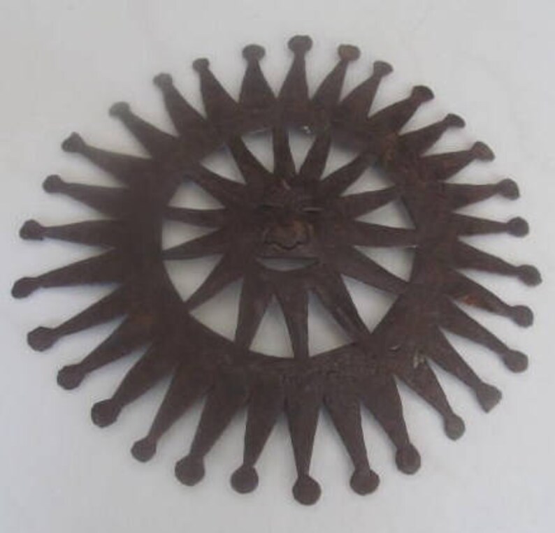 May include: A metal sun with a face and 16 rays, each with a pointed tip. The sun is a cutout design, with the face visible through the centre.