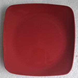 May include: A square, red dinner plate with a slightly rounded edge.