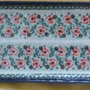 May include: A white ceramic serving tray with a blue and green border. The tray is decorated with a repeating pattern of red flowers and green leaves.