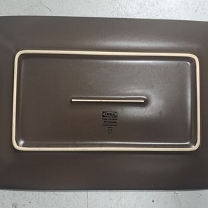 May include: A brown rectangular ceramic serving platter with a raised rim and a smaller rectangular inset. The platter has the IKEA logo and text that reads "Design and Quality IKEA of Sweden Made in Europe 1497".