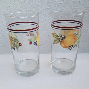 Puede incluir: Dos vasos de beber de vidrio transparente con una franja roja, azul y blanca alrededor de la parte superior. Los vasos tienen un diseño pintado de limones, hojas y bayas.