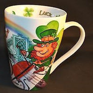May include: A white ceramic mug with a colorful design featuring a leprechaun playing a fiddle, a rainbow, shamrocks, and the word "Luck".