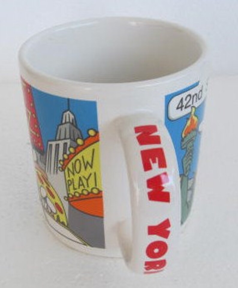 May include: White ceramic mug with a colorful illustration of New York City landmarks, including the Empire State Building, the Statue of Liberty, and a yellow taxi. The handle of the mug says "NEW YORK" in bold, white letters.