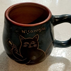 May include: A blue ceramic mug featuring a black cat design and the text "Nicaragua" on the side.