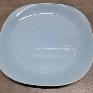 May include: A light blue ceramic dinner plate with a slightly rounded square shape.