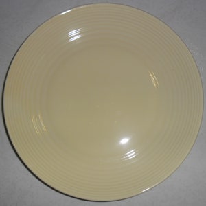 Peut inclure: Une assiette plate en céramique de couleur crème avec un motif de nervures sur le bord.