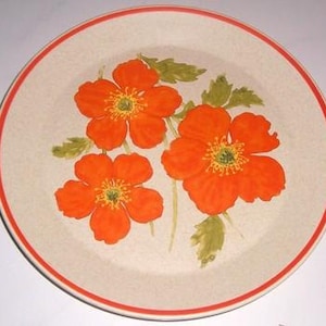 Op de afbeelding: Een beige keramisch dinerbord met een rode rand heeft een bloemmotief met drie oranje papaverbloemen met groene bladeren.