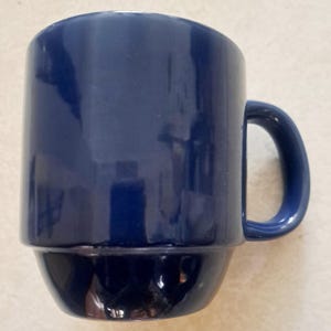 May include: A solid blue ceramic mug with a rounded handle. The mug has a slightly raised lip around the top.
